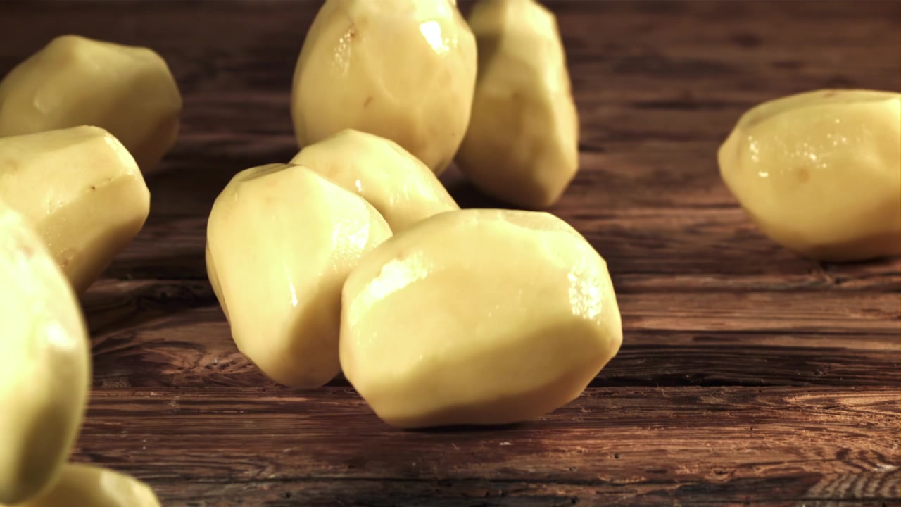 Patate pelate che cadono al rallentatore su un tavolo di legno rustico