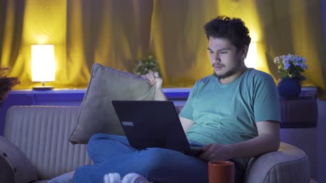 man watching horror movie on laptop at night. the man is frightened and tense.