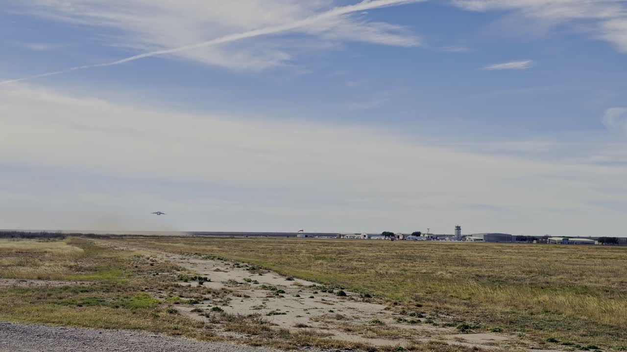 一架強大的C-17環球霸王III運輸機從遠處機場跑道起飛。飛機在蔚藍天空背景下爬升，揚起塵土，開始其旅程