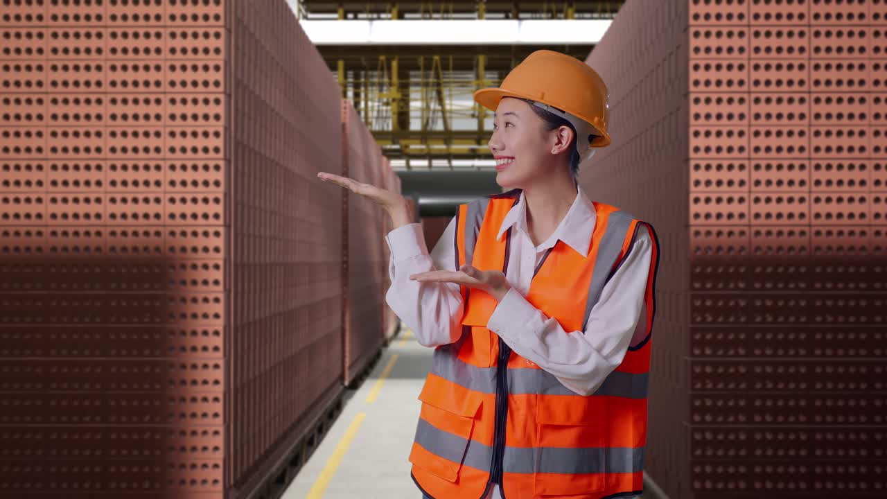 Asian Female Engineer With Safety Helmet Smiling And Pointing To Side While Standing With Red Brick Packed in Stacks Are Stored