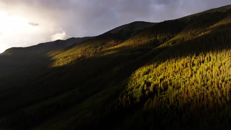 intense sunset and dynamic shadows over a mountainside covered in pine trees in colorado aerial dolly