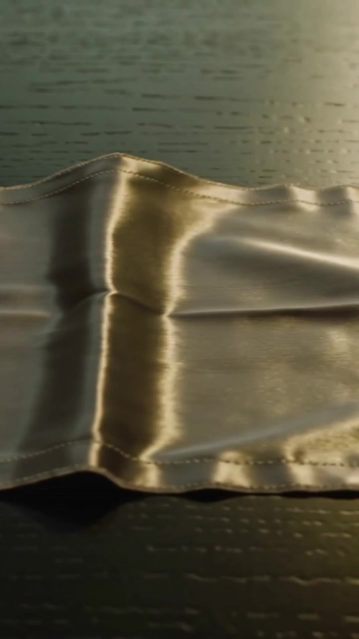 Vertical video: Relaxing satin panel forming ripples at center seam on wood table, right warm glow