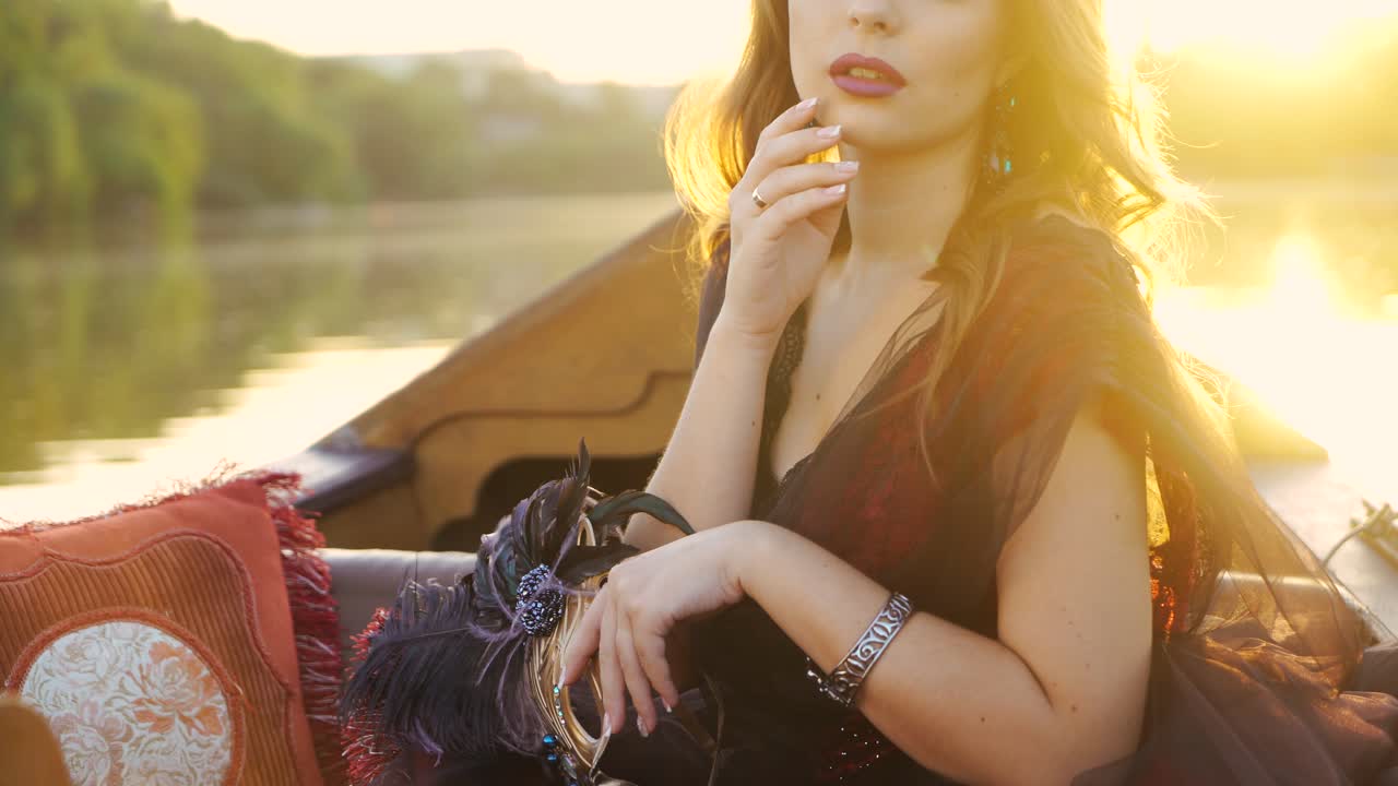A mysterious woman in effect dress is looking thoughtfully at the river in the gondola at sunset. Close-up. Blurred Background