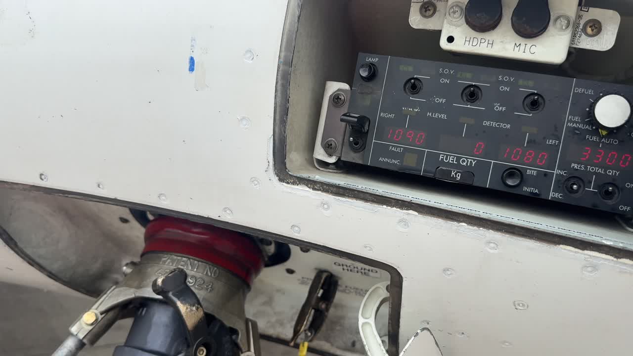 Close up view of a fuel hose connecting to the refuel polint of a jet airplane, with a view of the selector panel