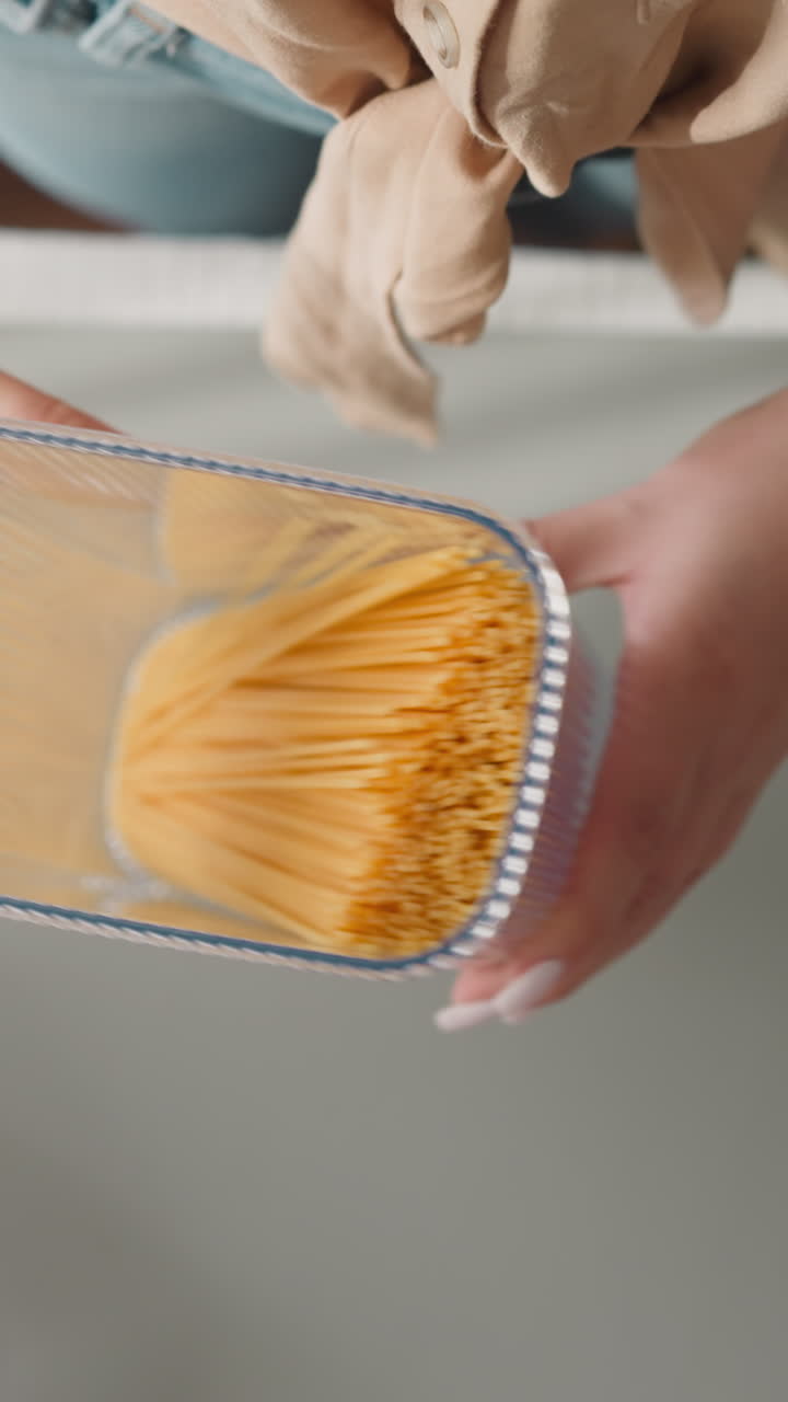 Young woman examines movement of raw spaghetti shaking plastic container slow motion. Lady distributes loose food products into special closed container upper view