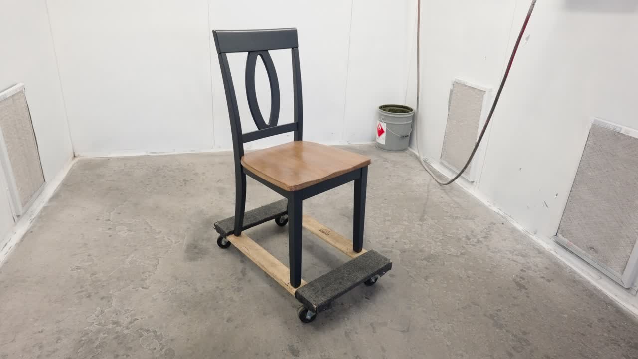 Camera slowly orbits grey wooden dining chair inside industrial spray booth