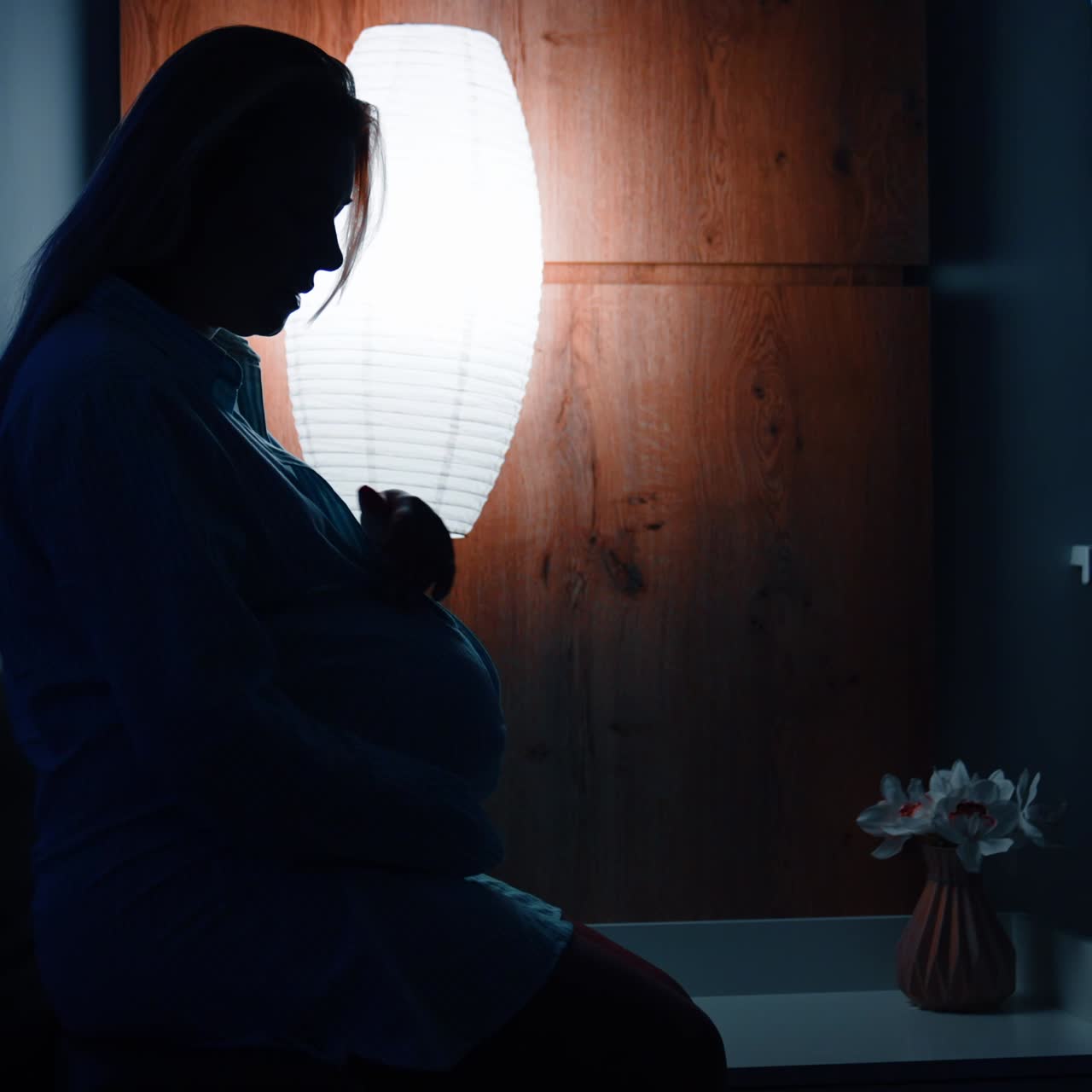 Silhouette of pregnant lady sitting on the bed in dark room. Woman strokes her big belly