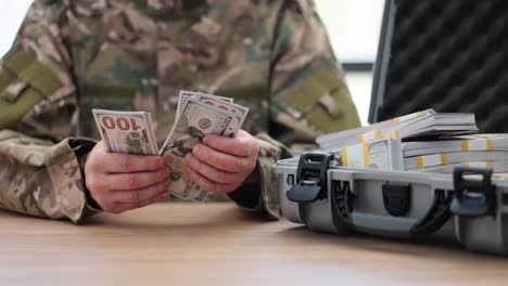 person in military uniform counting large stacks of us dollar bills