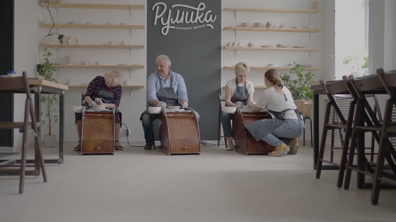 Woman master transfers knowledge to an elderly woman working on a potter's wheel and making a mug of ceramics in her workshop in slow motion