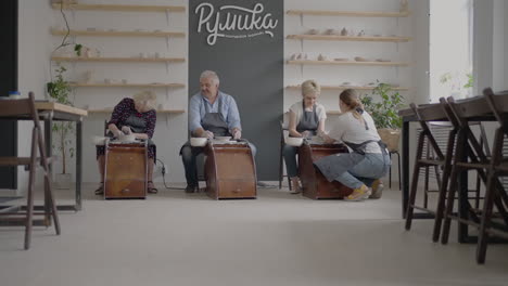 Woman-master-transfers-knowledge-to-an-elderly-woman-working-on-a-potter's-wheel-and-making-a-mug-of-ceramics-in-her-workshop-in-slow-motion