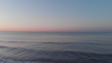 Dron-De-La-Puesta-Del-Sol-Del-Horizonte-Azul-Con-Olas-Serenas,-Orilla-Del-Horizonte-En-El-Mar