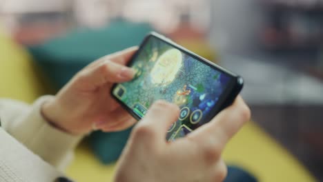 close up on hands playing an rpg strategy video game on a horizontally held smartphone at home living room. feminine hands tapping the mobile phone screen with a colorful game over the internet.