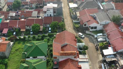 White-car-driving-through-local-Indonesian-neighborhood-of-Bandung-at-sunrise,-aerial