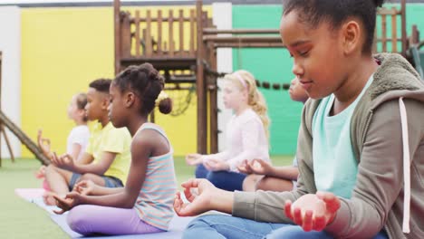 diverse schoolchildren exercising and meditating on mats at school playground