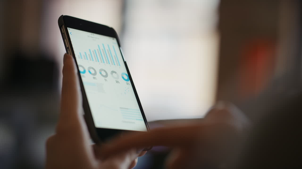 Close up of womans hands using smart phone to read business graphs