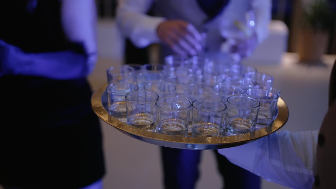 Close up of a tray with filled shot glasses being served at an event under vibrant lighting