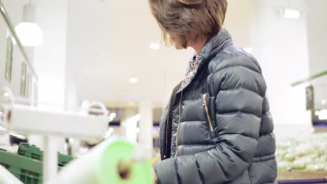 mujer joven comprando en la tienda de comestibles eligiendo verduras y frutas