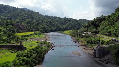hombre arrastra la madera contrachapada lentamente a través del puente colgante cruzando un río ancho, estática aérea