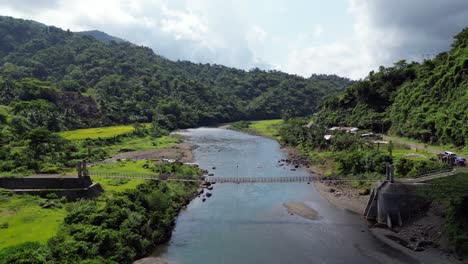 man drags plywood slowly across suspension bridge crossing wide river, aerial static