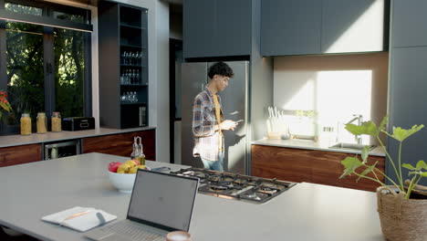 using smartphone, teenage boy standing in modern kitchen with laptop on counter
