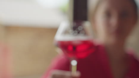 close up of people celebrating with glasses of red drink and ice cubes during toast, blurred background adds soft focus to cheerful moment shared in bright setting