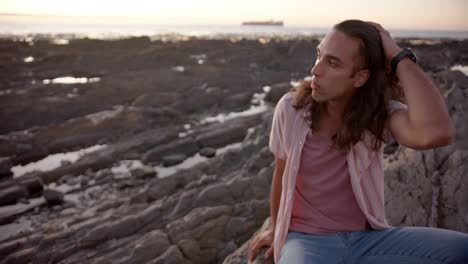 Happy-biracial-man-sitting-on-rock-at-beach,-slow-motion