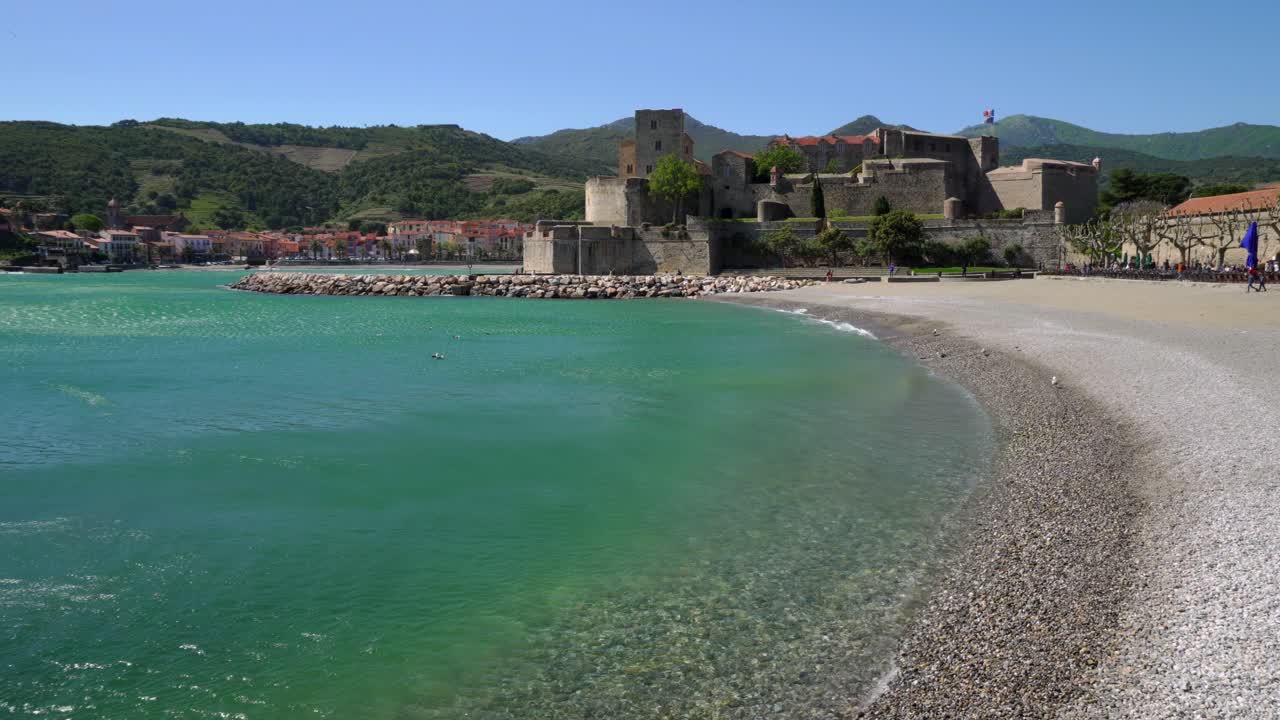 La spiaggia e il castello di Collioure in una giornata calda e ventosa, con il vento che sferza l'acqua del mare nella baia.