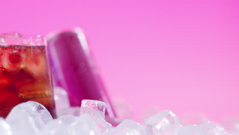 close up of chilled cold drink in glass poured from can on ice cubes against pink background 1