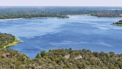 Volando-De-Regreso-A-Través-De-Una-Sección-De-árboles-Que-Abarca-Una-Sección-Azul-Brillante-Del-Lago