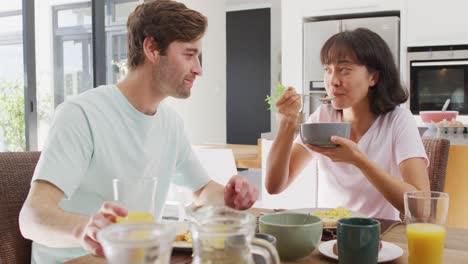 video of happy diverse couple eating breakfast together in kitchen