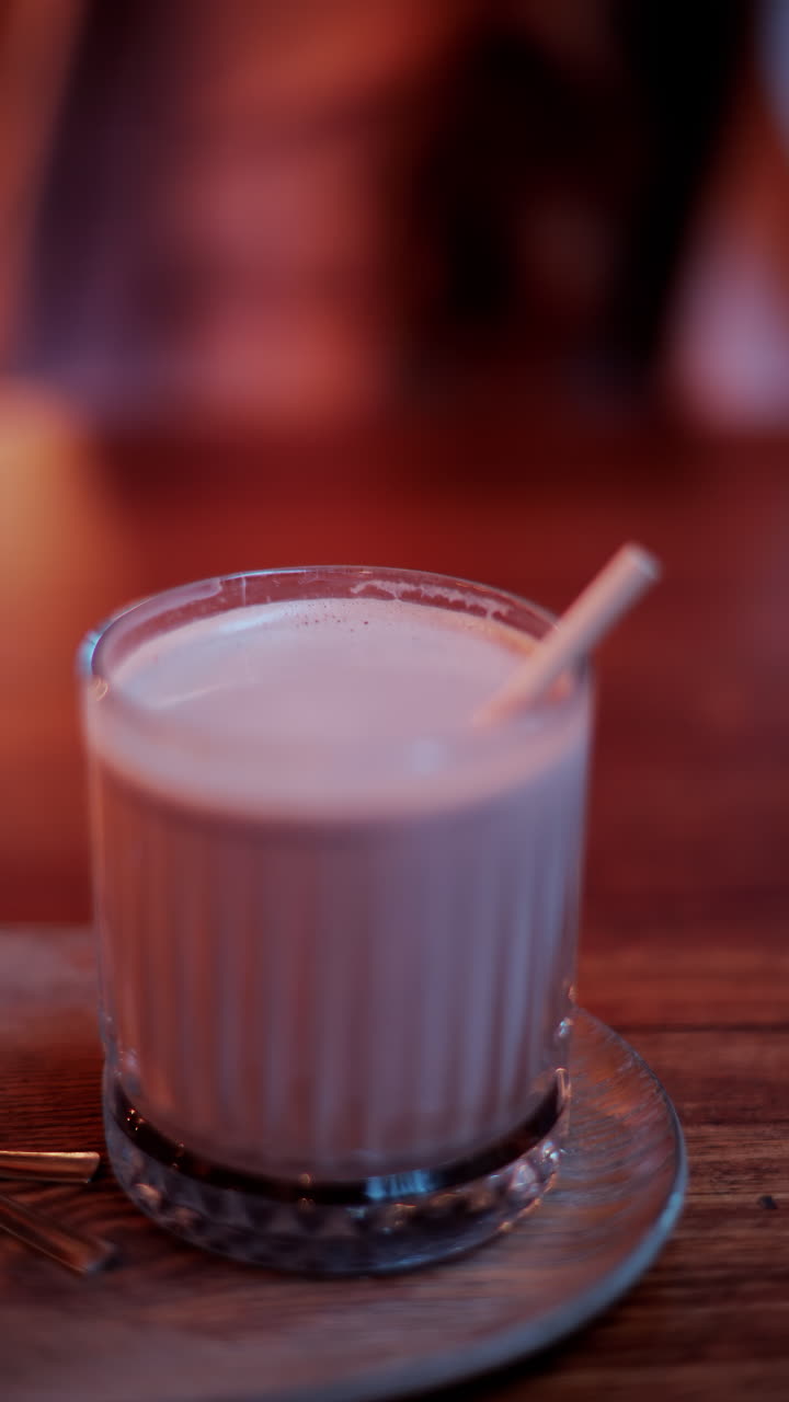 Close up of a hot chocolate in a glass with a straw on a table at a cafe. Vertical