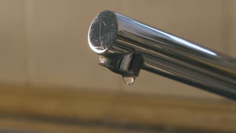 una gota de agua cae del grifo del fregadero en cámara lenta, detalle del grifo