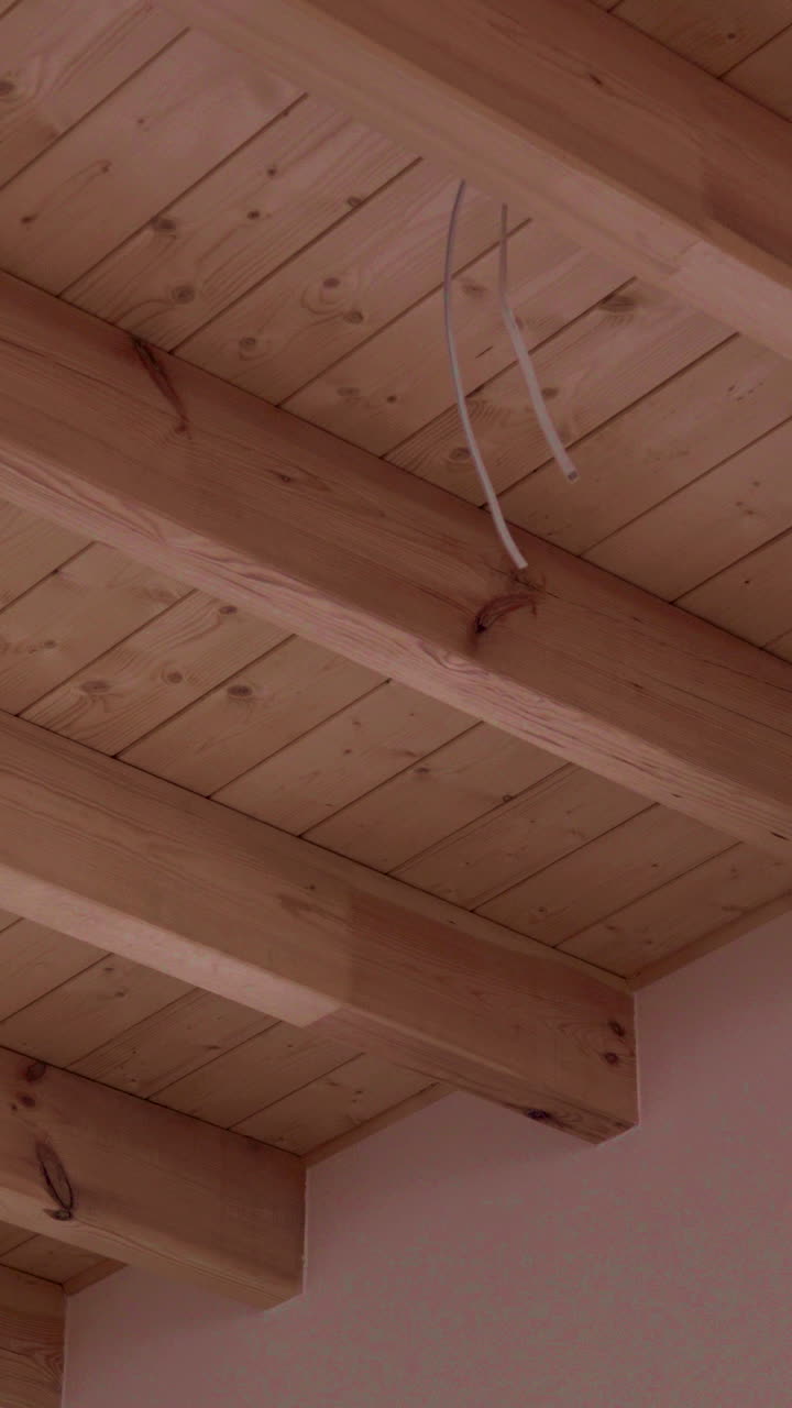 A closeup view of a wooden ceiling featuring exposed beams and visible wiring. Ideal for architectural studies, interior design projects, construction themes, and home renovation visuals