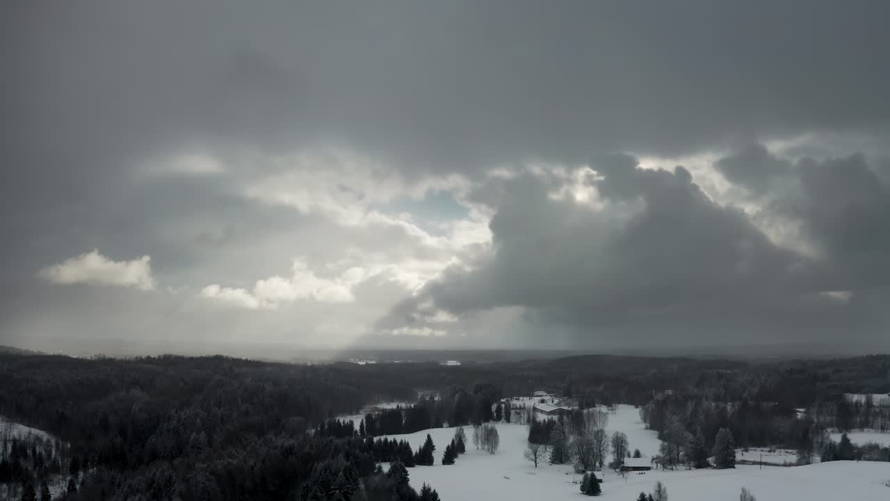 Aerial drone view of dramatic sky over the forest with sun rays breaking through the clouds and snow falling over a forest in countryside landscape. Frozen forest trees in winter.