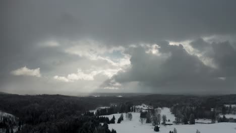 aerial drone view of dramatic sky over the forest with sun rays breaking through the clouds and snow falling over a forest in countryside landscape. frozen forest trees in winter.