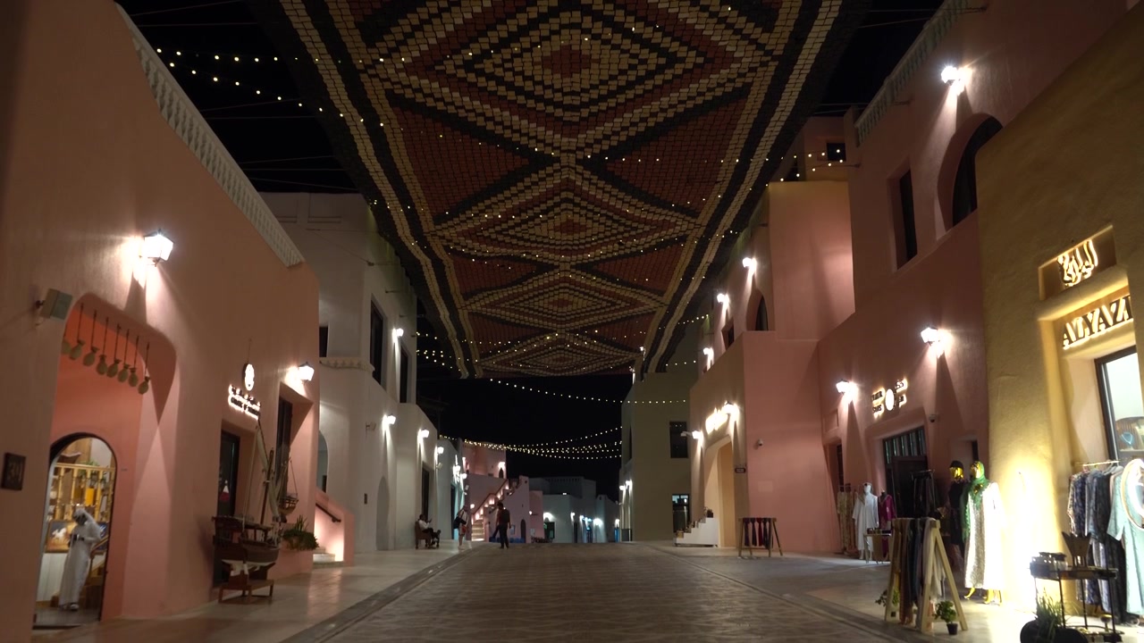 Ripresa in movimento che rivela una strada splendidamente illuminata in un tradizionale mercato arabo di notte, mettendo in risalto l'architettura unica, le vetrine luminose e le decorazioni culturali sul soffitto