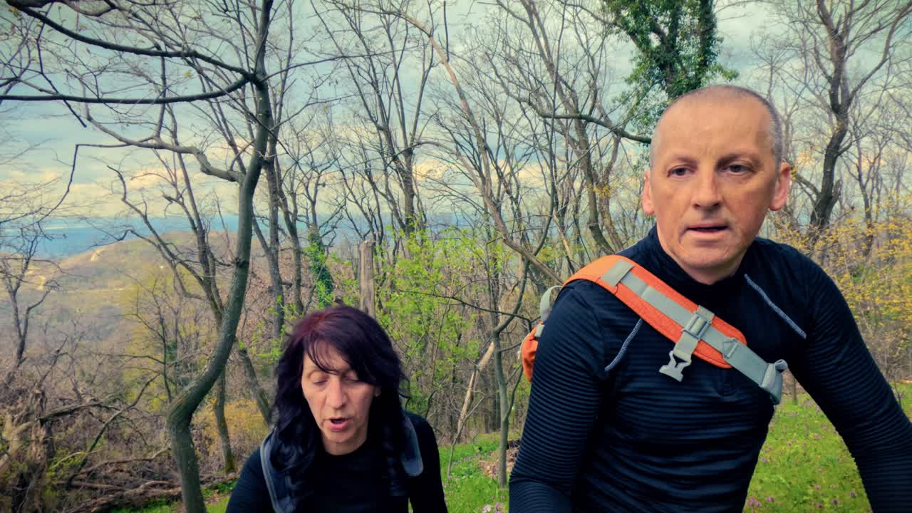 Coppia di mezza età che fa trekking insieme in un bosco fiorito primaverile. Concetto di invecchiamento sano, rimanere attivi, forma fisica e vitalità nella natura.