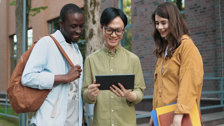 Camera zooming on caucasian woman, asian and african american students talking while looking at the tablet in the street near the college