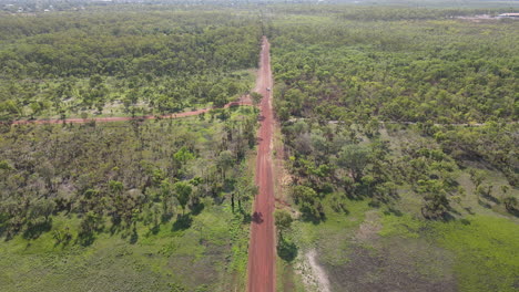 toma aérea de alto movimiento lento de un largo camino rojo recto y matorrales verdes cerca del parque natural de la jungla de holmes, darwin, territorio del norte