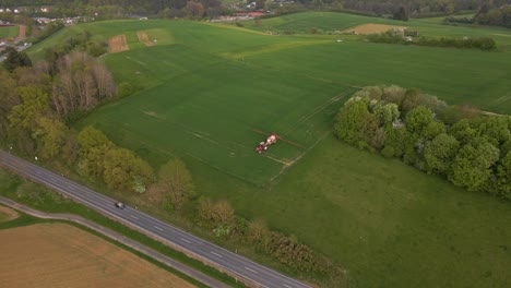 aerial footage of a large meadow in the german hesse region where a farmer is driving his tractor with water and a sprinkler