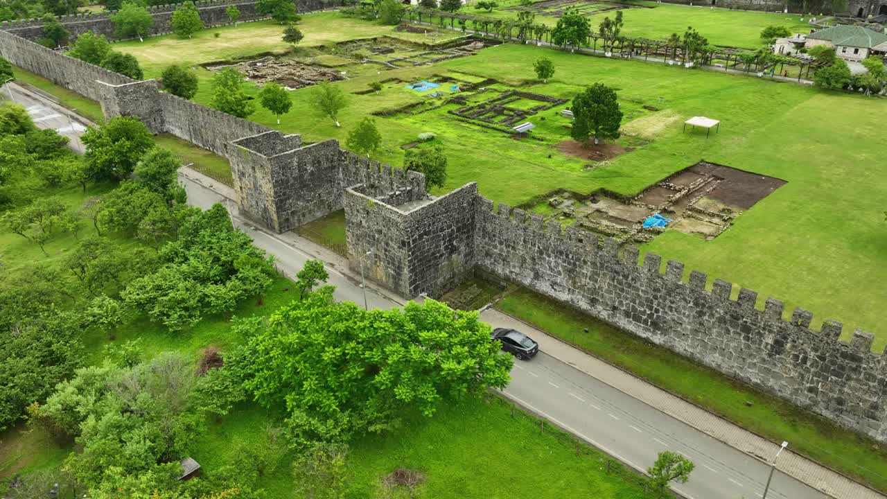 The thick stone walls of the ancient fortress stretch along the green hillside, a perfect harmony of history and nature