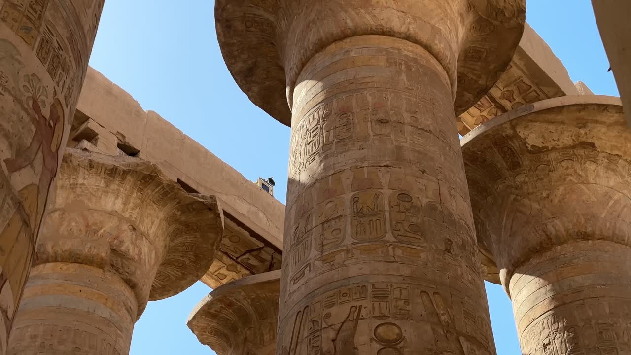 Ripresa cinematografica dal basso di colonne monumentali in pietra con rilievi colorati e notevolmente conservati e iscrizioni geroglifiche nella Grande Sala Ipostila del Tempio di Karnak, Luxor, Egitto.
