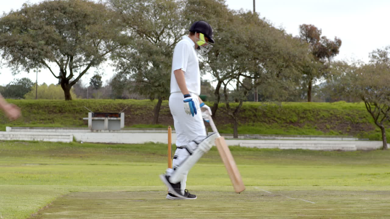 Playing cricket, bowler in white uniform walking towards stumps on field
