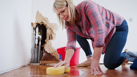 mature woman at home mopping up water from leaking pipe