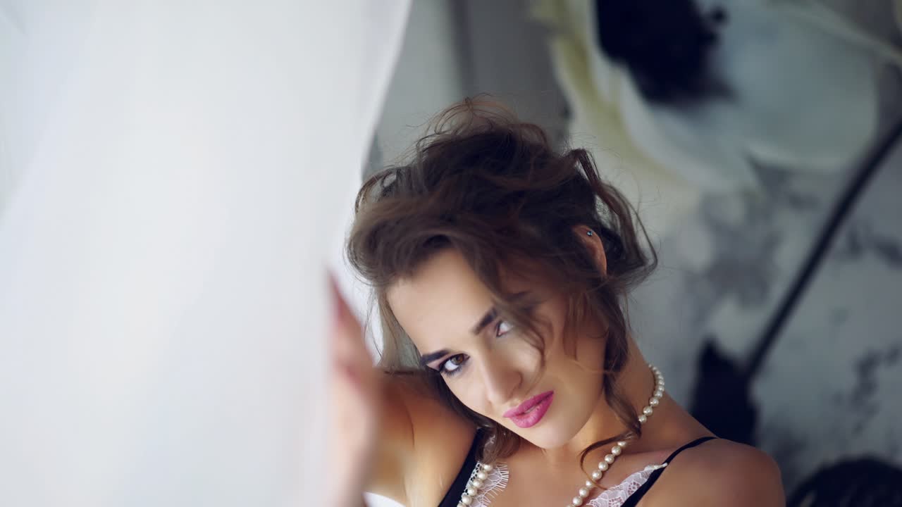 Portrait of beautiful young woman posing near the window. Portrait of beautiful tender young woman with long hair in lace lingerie posing near the window