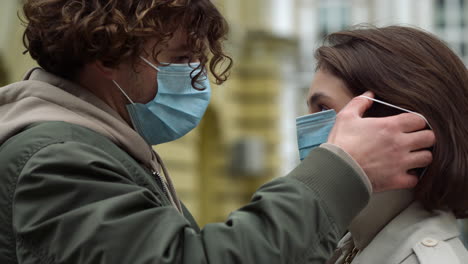 affectionate couple wearing face masks outdoor. man putting mask on girlfriend.