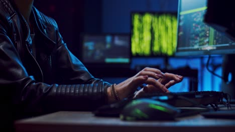 close up of the young female hacker or software developer in glasses tapping, typing and texting on the keyboard of computer at night while programming and coding