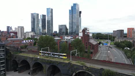 Luftdrohnenflug-Neben-Einer-Straßenbahn-Auf-Einer-Brücke,-Der-Einen-Hintergrund-Von-Wolkenkratzern-Und-Wohnhäusern-Im-Stadtzentrum-Von-Manchester-Zeigt