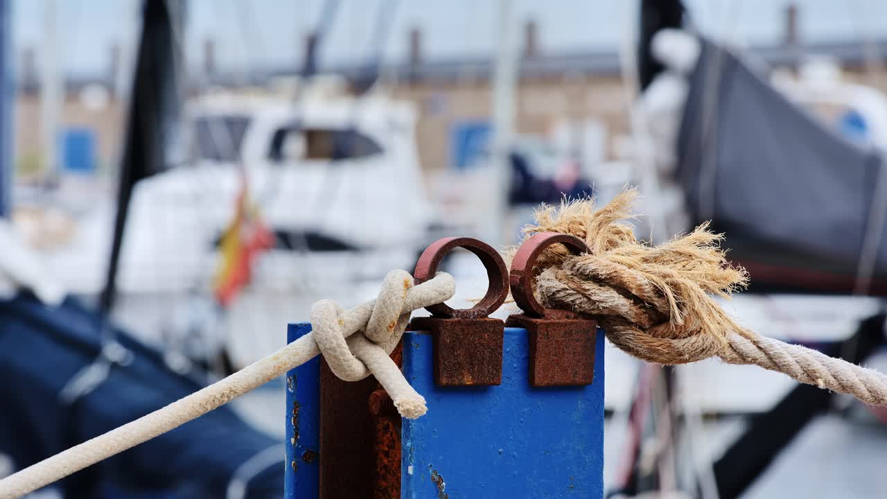 Ropes tightly knotted on dock pole with blurred marina boats in background, 4K