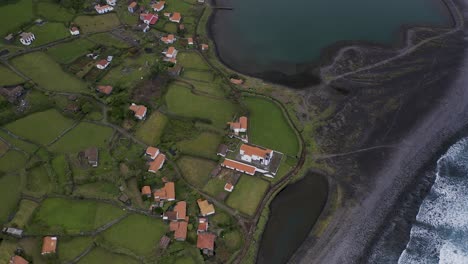 drone top down boom view of a coastal village lush green landscape, fajã de santo cristo, são jorge island, the azores, portugal